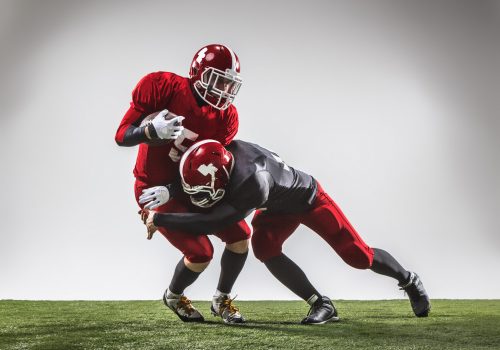 The two american football players in action on green grass and gray background.